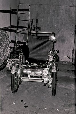 Vintage sidecar motorcycle with exposed engine and dual wheels, parked in a dimly lit garage. Sidecar features a fabric seat ...