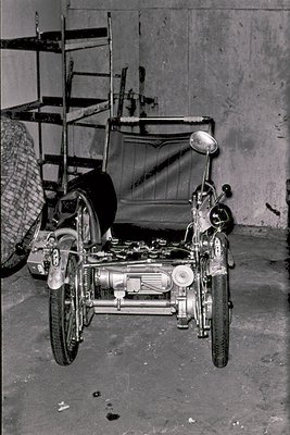 Vintage sidecar motorcycle with exposed engine and chain drive, parked in an industrial garage. Sidecar features a canvas cov...