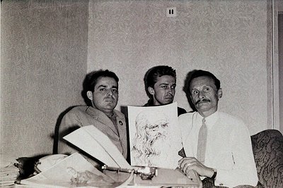 Black-and-white portrait of three men in formal attire (1960s-70s) holding a charcoal sketch of a bearded face. Plain wall an...