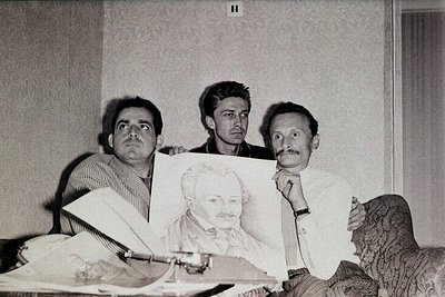 Three men pose indoors with a hand-drawn portrait of a bearded figure, likely a public leader, from the 1960s–70s. Mid-centur...