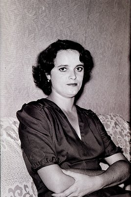 Portrait of a woman in a 1950s-style dress with a deep V-neck and puffed sleeves, seated with crossed arms. Floral-patterned ...