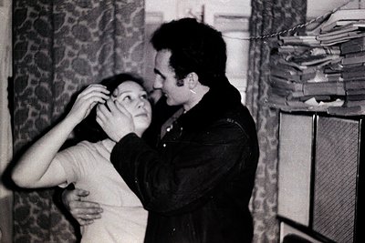 Intimate black-and-white moment of two people dancing closely indoors, likely mid-1960s–70s. Man in dark jacket adjusts woman...