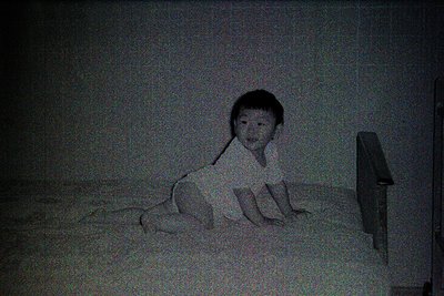 Vintage sepia-toned portrait of a young child lying on a bed, head propped on a pillow. Soft focus and muted lighting evoke n...