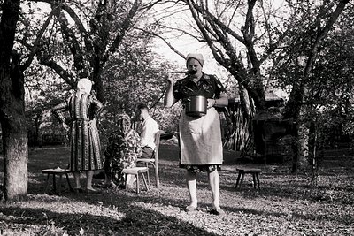 Mid-20th century rural scene featuring three women in traditional folk attire. Central figure wears a patterned headscarf and...