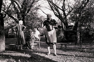 Three women in traditional folk attire pose outdoors in a rural setting, mid-20th century. Left: striped dress with apron, he...