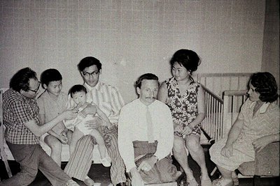 Black-and-white group portrait of seven individuals in a modest indoor setting, likely a 1970s hospital or clinic. Central fi...