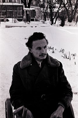Mid-century man in winter coat and scarf sits on a metal bench in snow-covered park. Classic 1950s–1960s hairstyle and attire...