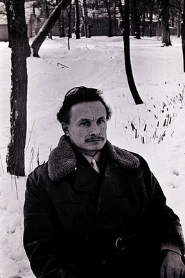 Mid-century man in a fur-collared coat poses against a snow-dusted forest, 1950s–60s style. Classic winter portrait with barr...