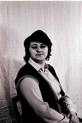 Portrait of a woman in a mid-century studio setting, wearing a sleeveless black vest over a collared shirt. Short, layered ha...