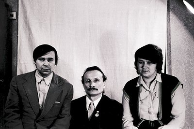 Three individuals pose formally in a studio setting, likely Eastern Bloc-era (1970s–1980s). Center figure wears a medal and s...
