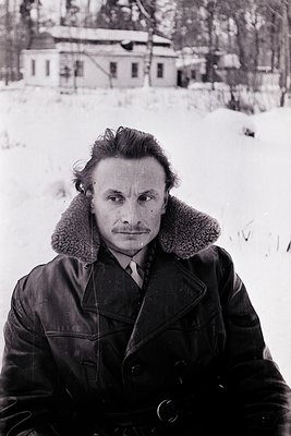 Portrait of a man in a winter coat with fur-lined collar, standing in snow-covered terrain. His hairstyle and attire suggest ...
