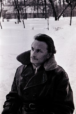 Mid-century portrait of a man in a winter coat with fur collar, standing on snow-covered ground. His expression is contemplat...