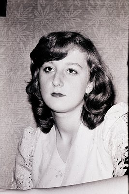 Portrait of a woman with voluminous 1960s-style side-parted hair and subtle makeup, wearing a lace-trimmed blouse. Soft focus...