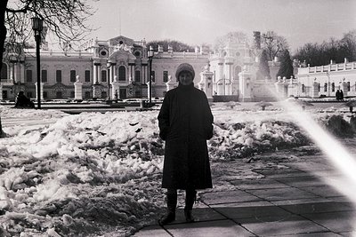 Neoclassical palace courtyard blanketed in snow, with a lone figure in winter attire standing near a frozen fountain. Archite...