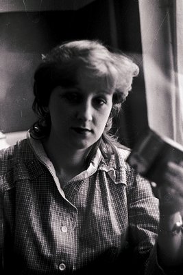 Portrait of a young woman in a checkered blouse, mid-20th century style. Soft focus and indoor lighting suggest a candid or d...