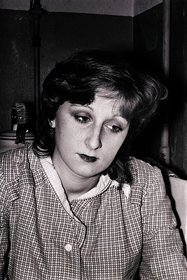 Portrait of a woman in a checkered blouse, shot in black-and-white. Her short, voluminous hair and subtle makeup suggest a mi...