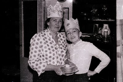 Vintage black-and-white photo of a woman and child in matching paper crowns, likely celebrating a birthday or holiday. The wo...