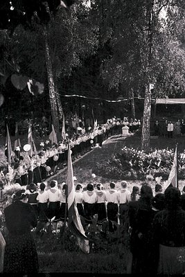 1960s outdoor gathering in a park, featuring rows of seated attendees in formal attire. Decorated with floral arrangements, f...