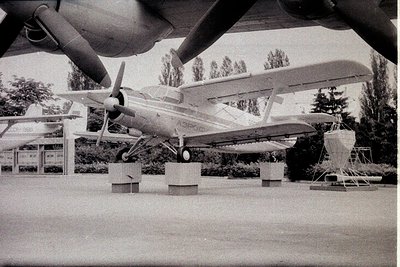 Retro single-engine propeller plane displayed indoors, elevated on concrete supports. High-wing monoplane with visible landin...