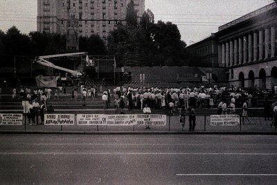 Crowd demonstration in an urban setting, likely Eastern Europe, 1980s. Barricades with Cyrillic text and banners in Cyrillic ...