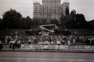 Crowd demonstration with construction crane in foreground, surrounded by handwritten banners in Cyrillic. Soviet-era high-ris...