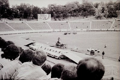 Vintage stadium shot featuring a midfield obstacle course with a crane and vehicles, likely from the 1960s-70s. Crowd in tier...