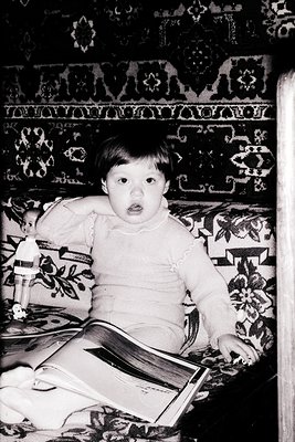 Young child in 1970s-style sweater reading a book on an intricately patterned sofa, likely Eastern European interior. Floral ...