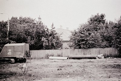 Mid-20th century industrial site featuring a Soviet-era **D-20 bulldozer** (marked "120") clearing land. Stacked concrete pip...