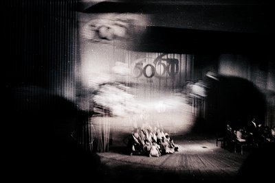 Vintage black-and-white shot of a crowded theater interior, likely from the 1950s–1960s. Motion blur captures a performer’s d...