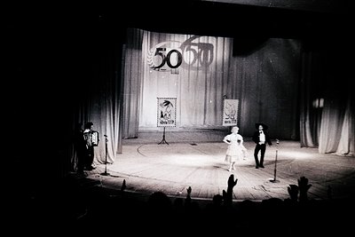 Black-and-white stage performance celebrating Bulgaria’s 50th anniversary (1964), featuring a woman in a vintage gown and man...