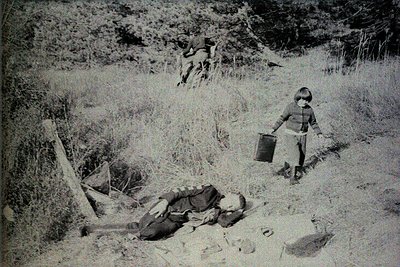 Mid-20th century rural scene: a child in striped sweater and shorts carries a metal bucket, while another child lies on the g...