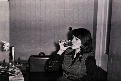 Vintage black-and-white portrait of a woman in a cozy indoor setting, holding a glass of wine. She wears a patterned sweater ...
