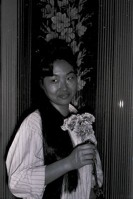 Portrait of an individual in traditional attire holding a bouquet of white flowers, likely chrysanthemums. The floral headpie...