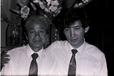 Black-and-white portrait of two men in formal attire—older man in a suit with a patterned tie, younger man in a white dress s...