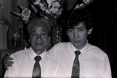Black-and-white portrait of two men in formal attire, likely 1970s–1980s. Older man in a light-colored suit with a patterned ...