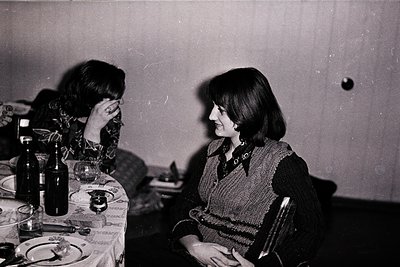 Two women seated at a table in an indoor setting, likely mid-20th century. The woman on the right wears a patterned sweater a...