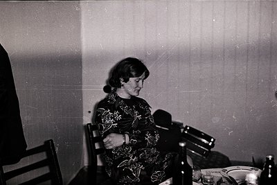 Vintage black-and-white photo of a woman seated at a table, wearing a floral-patterned blouse and dark skirt, engaged in conv...