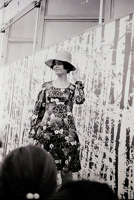 1960s fashion runway model in floral-patterned dress and wide-brim hat, striking a pose against a textured backdrop. Classic ...