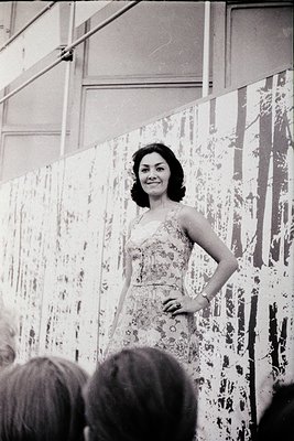 Vintage black-and-white portrait of a woman in a floral dress, posing confidently on a stage with abstract, textured backdrop...