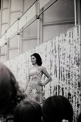 Vintage black-and-white portrait of a woman in a sleeveless floral dress, posing confidently in front of an abstract splatter...