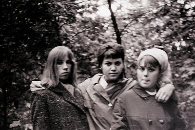 Three young women pose closely in a wooded area, likely late 1960s–early 1970s. Left: long, straight hair; center: short bob ...