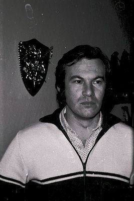 Black-and-white portrait of a man in a 1970s-style sweater with black-and-white stripes, posed indoors near a mirror reflecti...