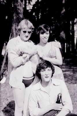 Black-and-white candid of three individuals in casual summer attire—man in sunglasses and rolled-up sleeves, woman in sleevel...