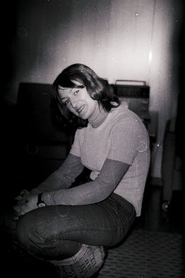 Vintage black-and-white portrait of a person seated on a patterned carpet, wearing a striped long-sleeve shirt and distressed...