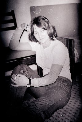 Vintage black-and-white portrait of a person in a relaxed pose, seated on a wooden chair with a striped sweater and cuffed tr...