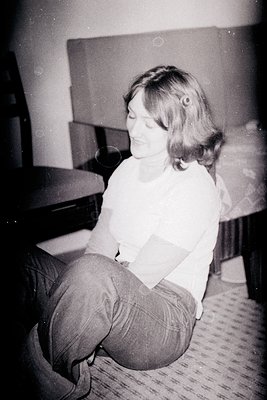 Vintage black-and-white portrait of a person seated on a patterned carpet, holding a book or magazine. Mid-century interior w...