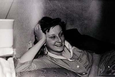 Vintage black-and-white portrait of a woman in a checkered blouse, resting her hand on her head with a relaxed smile. Indoor ...