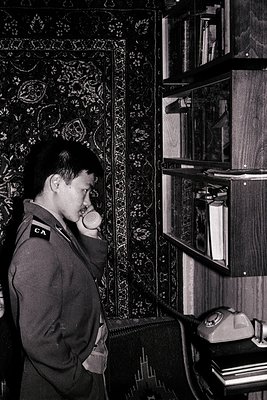 Mid-20th century interior: uniformed man (CA insignia) speaks into a rotary phone in a room with ornate patterned wallpaper a...