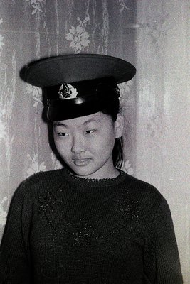 Black-and-white portrait of an individual in a military-style cap with an insignia, likely from the 1960s–1980s. The cap feat...