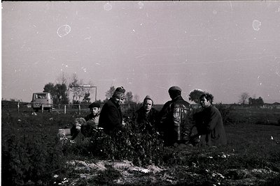 Vintage black-and-white photo of five individuals seated/standing in a rural field, likely mid-20th century. Traditional clot...